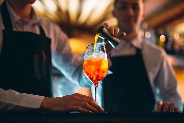 Foto mão de barman mexendo um coquetel de verão laranja fresco e doce com uma colher no balcão do bar.