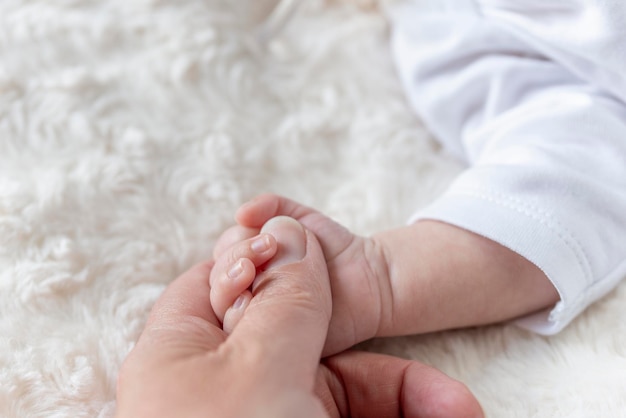 Mão de bebê recém-nascido segurando o dedo da mãe na cama