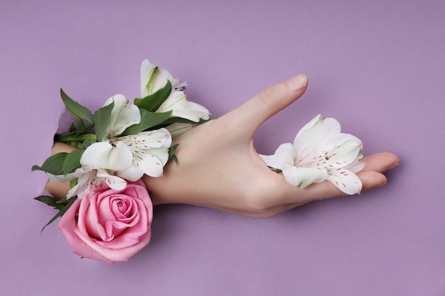 Mão de beleza com flores em um buraco em um papel roxo