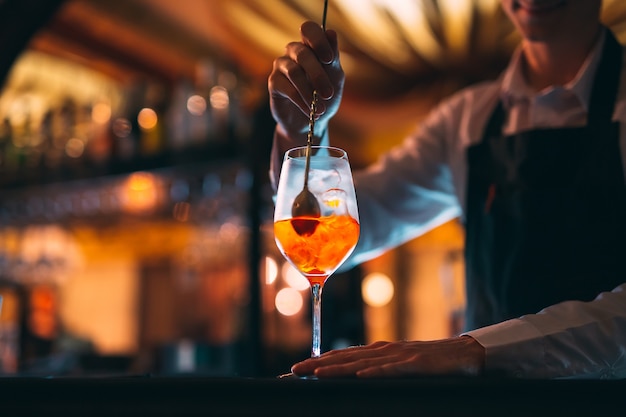 Mão de Braga, mexendo um cocktail de verão laranja doce e doce com uma colher no balcão do bar