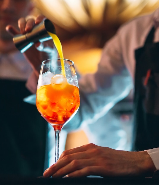 Mão de Braga, mexendo um cocktail de verão laranja doce e doce com uma colher no balcão do bar