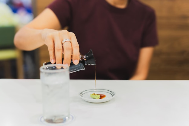 Mão de cliente de mulher derramando molho de soja japonês em wasabi em prato pequeno