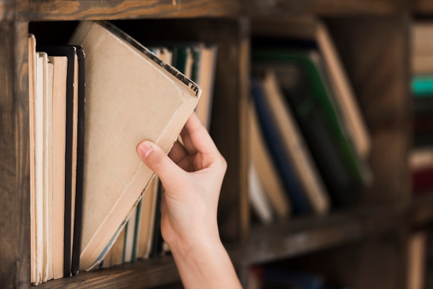 Mão de close-up, levando o livro de história da estante