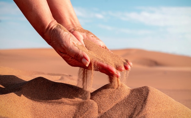 Mão de close-up liberando areia caindo. Areia fluindo pelas mãos contra o deserto dourado. Férias de verão.