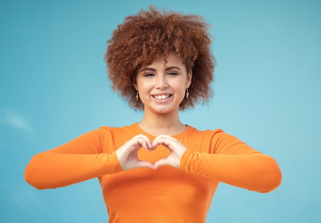 Foto mão de coração e retrato de mulher em estúdio por amor feliz e sorriso contra o espaço de fundo azul emoji mãos e rosto de modelo de menina relaxam com moldura de dedo e mensagem amorosa gesto e sinal