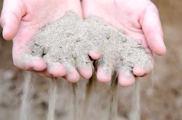 Mão de criança segurando a gota de areia no chão. Símbolo para passar tempo ou terra seca