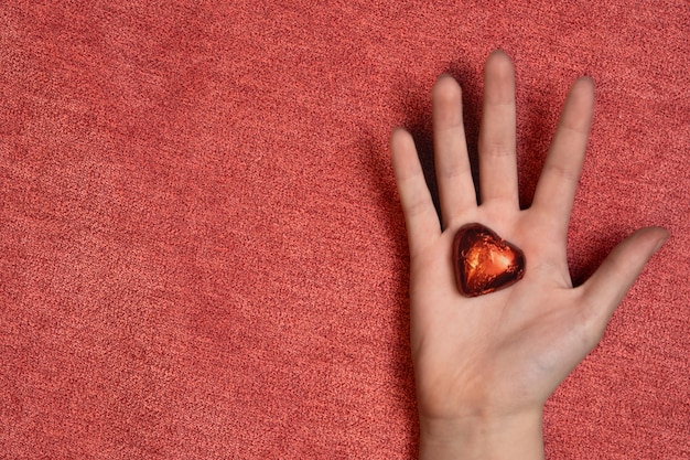 mão de criança segurando um chocolate vermelho em forma de coração