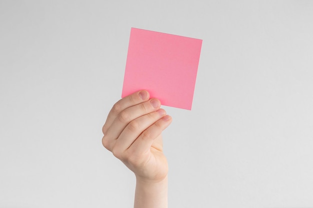 Foto mão de criança segurando um lembrete em branco quadrado rosa ou notas de papel acima de um fundo branco e cinza