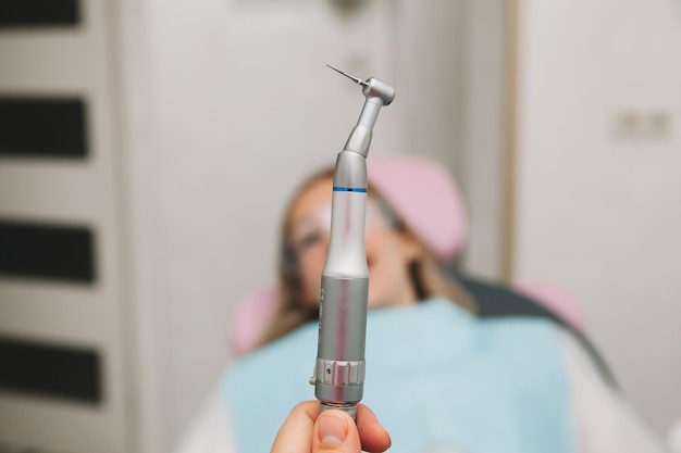 Mão de dentista segurando uma broca dentária com uma turbina. paciente em segundo plano com a boca aberta.