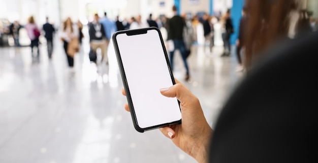 Mão de empresária segurando celular preto com tela branca em uma feira, copyspace para seu texto individual.