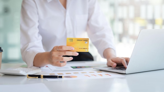 Mão de empresária segurando o cartão de crédito e usando o laptop Fechar o pagamento com cartão de crédito das mãos femininas Conceito de compras on-line