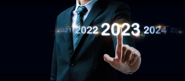 Foto mão de empresário de 2023 tocando e apontando no ano de 2023 com tela virtual em fundo escuro meta meta mudar de 2022 para 2023 estratégia investimento planejamento de negócios feliz ano novo conceito