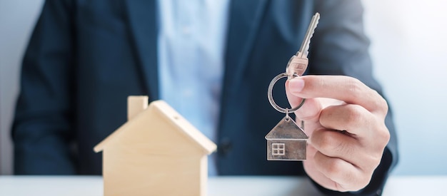 Mão de empresário segurando a chave com madeira modelo de casa Compra e venda de imóveis Aluguel de seguro de propriedade e conceitos de contrato