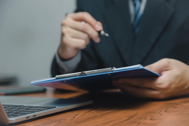 Mão de empresário segurando o relatório de gráfico de papelada de caneta e documento de marketing de investimento gráfico financeiro ou seguro fiscal na mesa