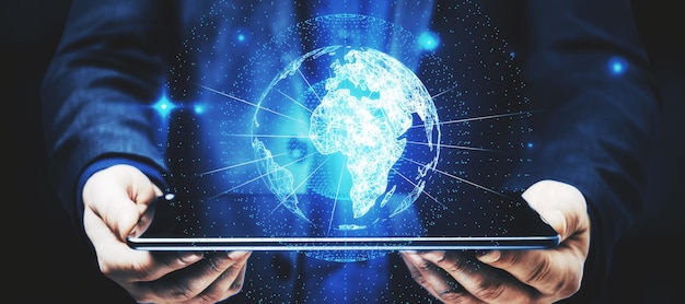 Mão de empresário segurando o tablet com holograma de globo brilhante sobre fundo azul Interface digital e inovação global
