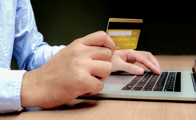 Mão de empresário segurando um cartão de crédito dourado com o laptop na mesa