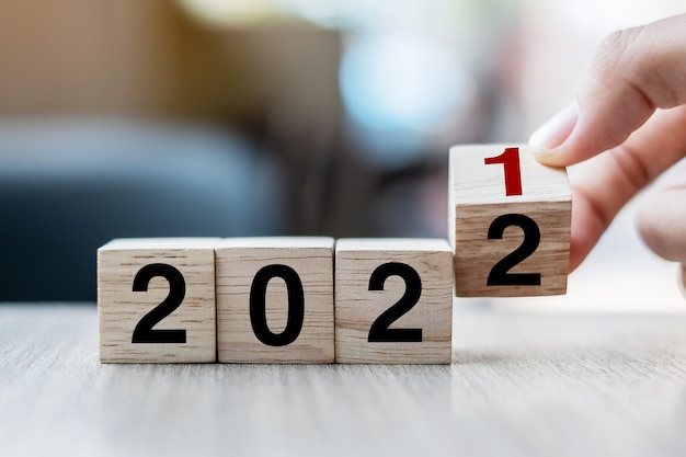 Mão de empresário segurando um cubo de madeira com virar o texto do bloco 2021-2022 no fundo da mesa. conceitos de resolução, estratégia, solução, objetivo, negócios e feriado de ano novo