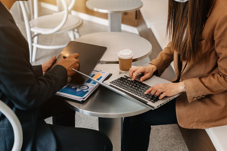 Foto mão de empresário usando smartphone, laptop e tablet com diagrama de rede social e dois colegas discutindo dados na mesa como conceito na luz da manhã.