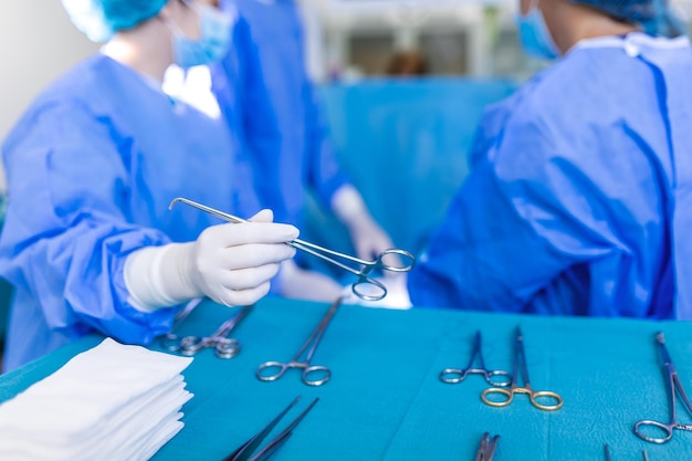 Mão de enfermeira tomando instrumento cirúrgico para grupo de cirurgiões no paciente operando em segundo plano no teatro cirúrgico Instrumentos médicos de aço prontos para serem usados Conceito de cirurgia e emergência