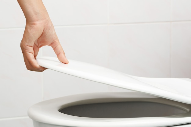 Mão de homem abrindo a tampa do vaso sanitário