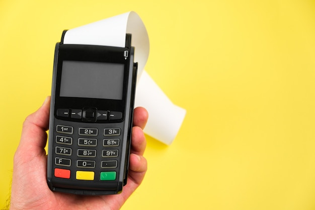 Mão de homem apertando um botão no terminal pos com fita adesiva em rolo de papel no fundo azul