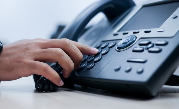 Mão de homem apontar para pressionar o número do botão na mesa de escritório de telefone