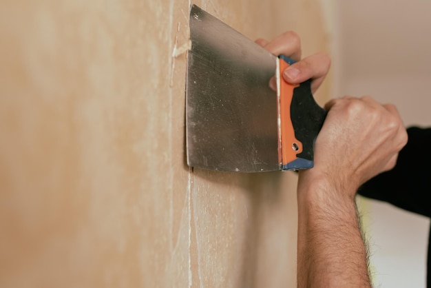 Mão de homem arrancando papel de parede antigo com raspador de parede