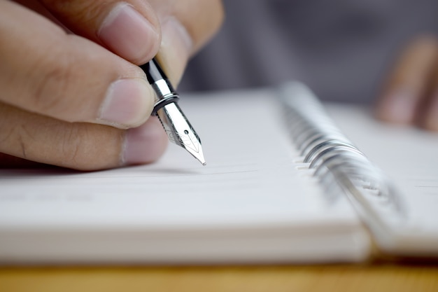 Mão de homem com caneta escrevendo no notebook