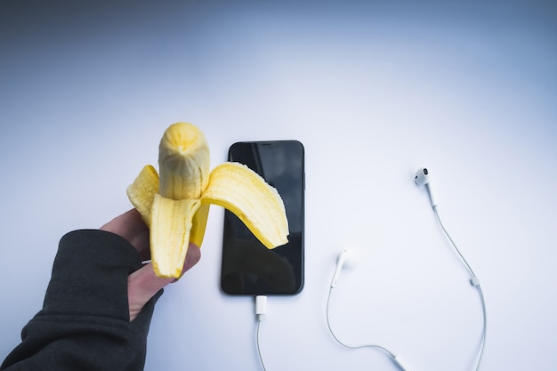 Mão de homem comendo banana antes de sair para correr com o smartphone