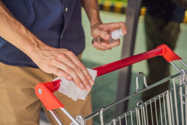 Foto mão de homem desinfetando carrinho de compras com spray de álcool para vírus corona ou proteção cobiçosa