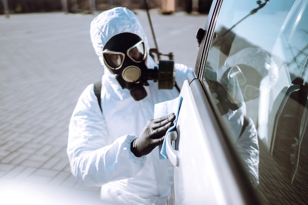 Mão de homem em alças de lavagem e desinfecção de traje de proteção de um carro.