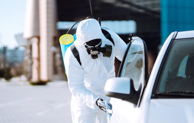 Mão de homem em roupas de proteção lavando e desinfetando alças de um carro