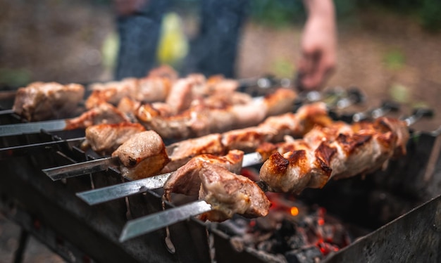 Mão de homem endireita o espeto de metal com churrasco deliciosa carne grelhada com fumaça no braseiro fora ...