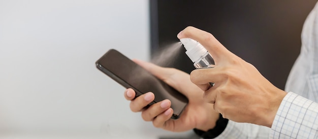 Mão de homem, pulverizando a garrafa de desinfetante de álcool para o Smartphone