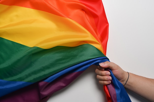 Mão de homem segurando a bandeira do orgulho lgbt em fundo branco. conceito lgbt.