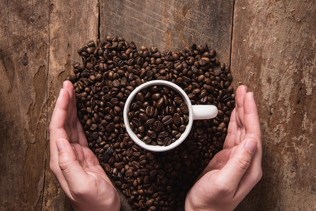 Mão de homem segurando a xícara de café e grãos de café na mesa de madeira