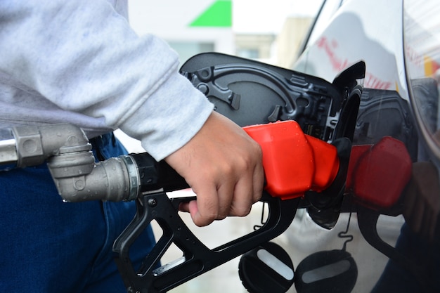 mão de homem segurando o bocal de abastecimento vermelho e combustível de gasolina de bombeamento preencha o carro no posto de gasolina