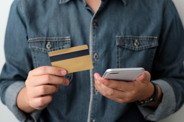 Mão de homem segurando o cartão de crédito e smartphone