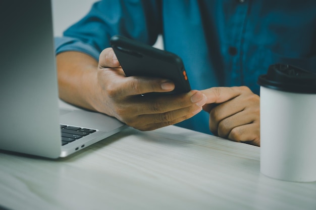 Mão de homem segurando smartphone e laptop de computador para tecnologia de trabalho pesquisando na internet enviando sms