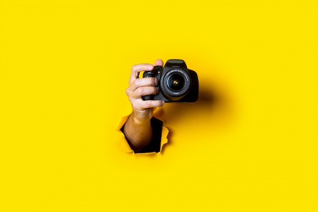 Mão de homem segurando uma câmera em um fundo amarelo brilhante