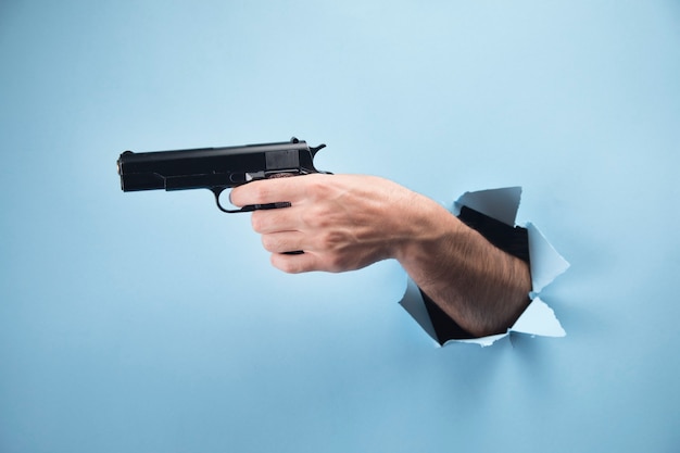 Mão de homem segurando uma pistola em uma cena azul