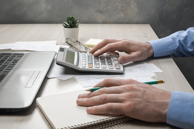 Foto mão de homem, usando a calculadora e escrever, faça anotações com calcular sobre custos e impostos no escritório em casa.