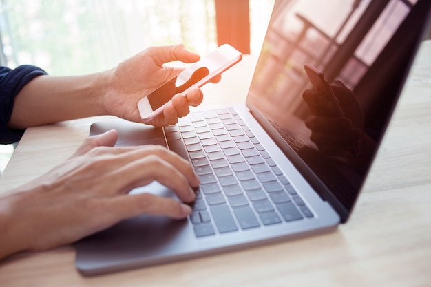 Foto mão de homem usando laptop e smartphone trabalhando remotamente em casa