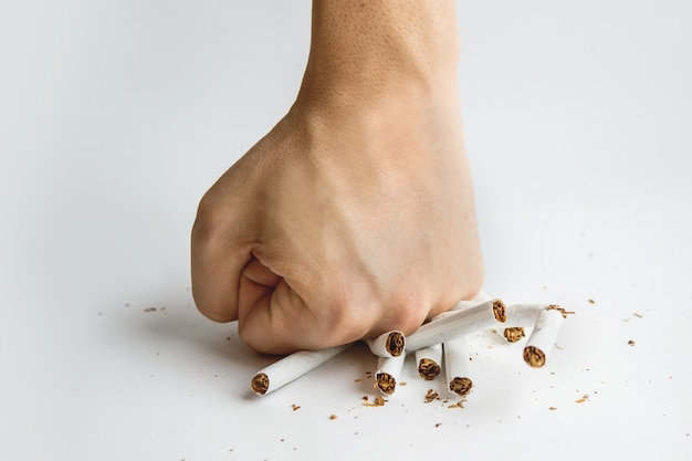 Mão de homens esmagou alguns cigarros, não fumar, parar de fumar e estilo de vida saudável. Cara quebra um cigarro com os dedos em fundo branco. Os malefícios do tabagismo. Parar de fumar.