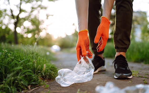 Mão de homens recolhe lixo plástico para limpeza no parque. O voluntário que usa luvas de proteção coleta o plástico da garrafa.