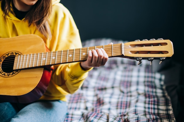 Mão de jovem closeup tocando violão em casa.