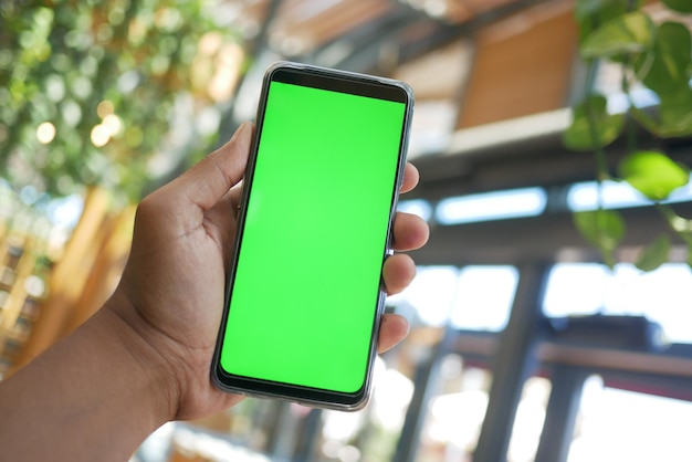 Mão de jovem usando telefone inteligente com tela verde no café