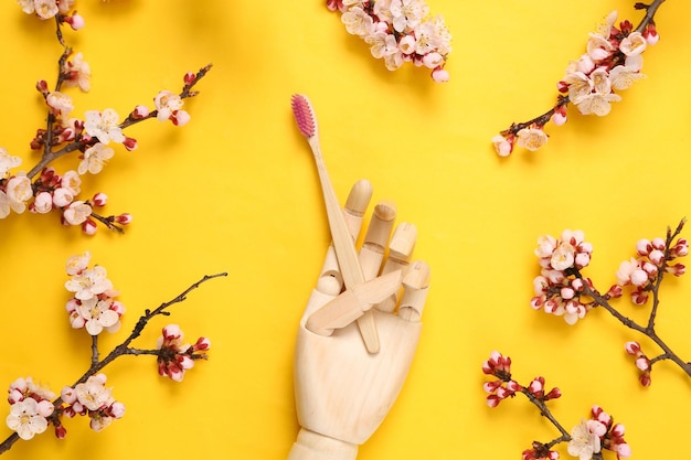 Mão de madeira segurando escovas de dente de bambu Eco e belos ramos floridos em fundo amarelo Conceito ecológico de primavera