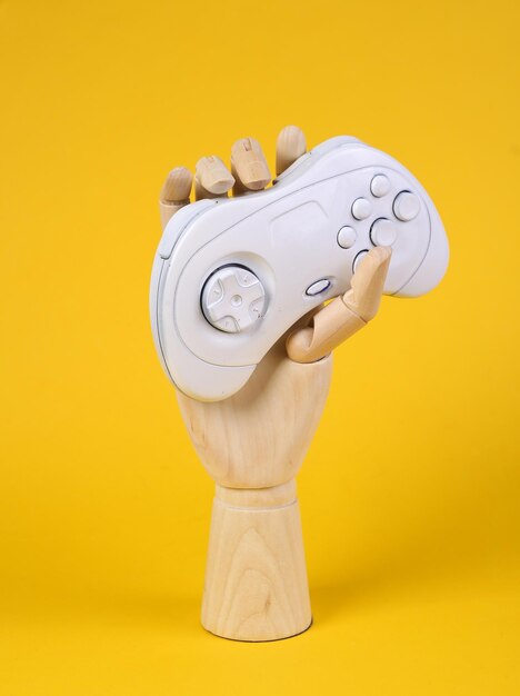 Mão de madeira segurando gamepad branco sobre fundo amarelo