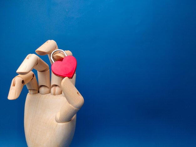 Foto mão de madeira segurando um cadeado de amor em um fundo azul